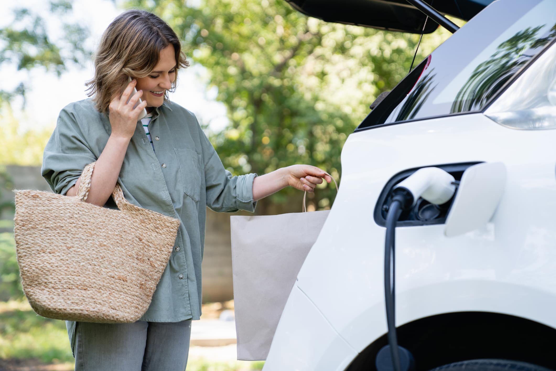 Woman with shopping bag next to a charging electric car consejos bateria coche electrico